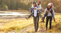 young couple giving their children piggy back rides through a field